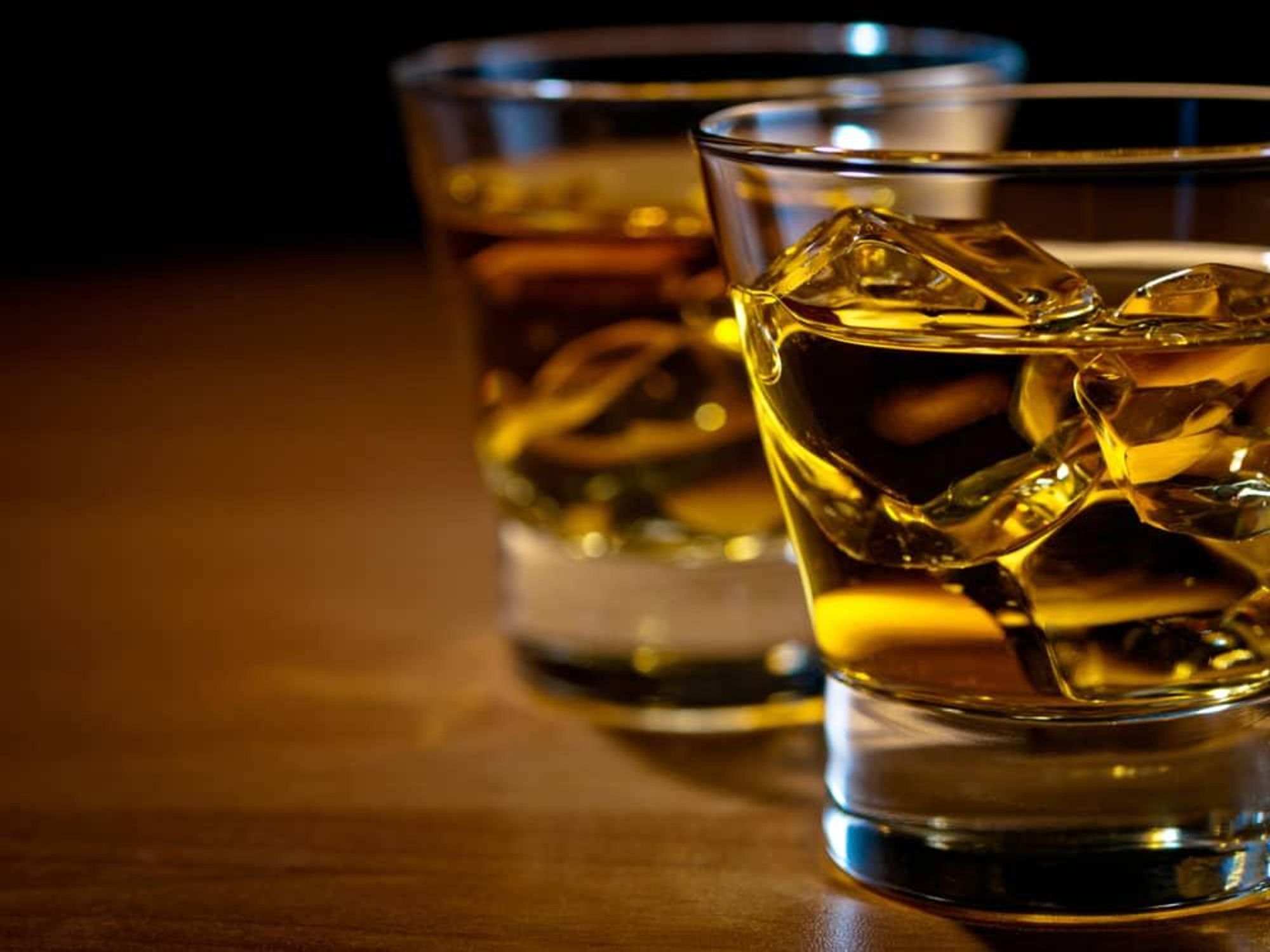 Glasses of whiskey with ice on bar or table