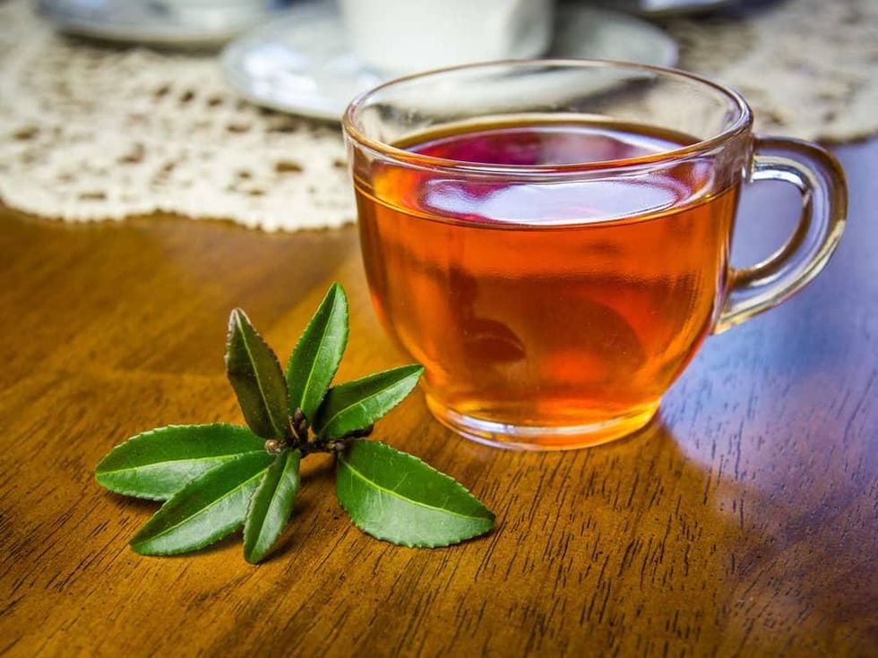 Photo of camellia sinensis leaves with cup of tea on table