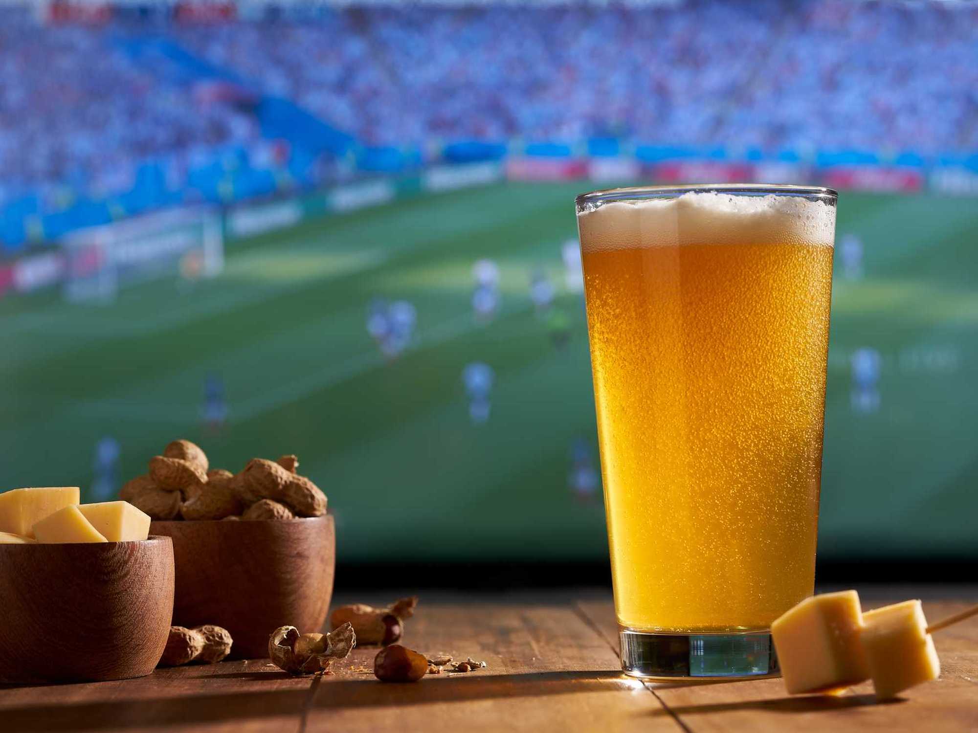 watching the soccer world cup on a large TV with a glass of beer, peanuts and cheese